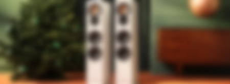 Two elegant white speakers are positioned next to a decorated Christmas tree in a cozy living room setting.