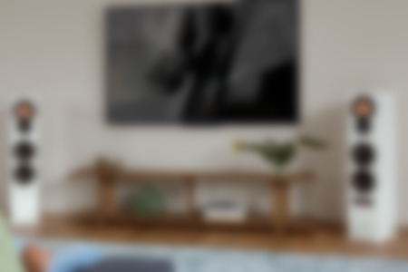 Osoba relaksuje się na sofie, ciesząc się muzyką z eleganckich białych głośników stereo Ultima 40 Aktiv Mk3 obok nowoczesnego telewizora.