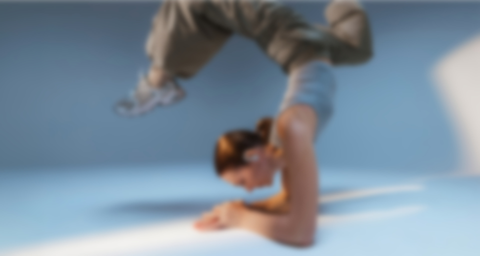 Une personne en tenue de sport fait un poirier sur le sol du gymnase tout en portant des écouteurs sans fil AIRY SPORTS TWS 2.