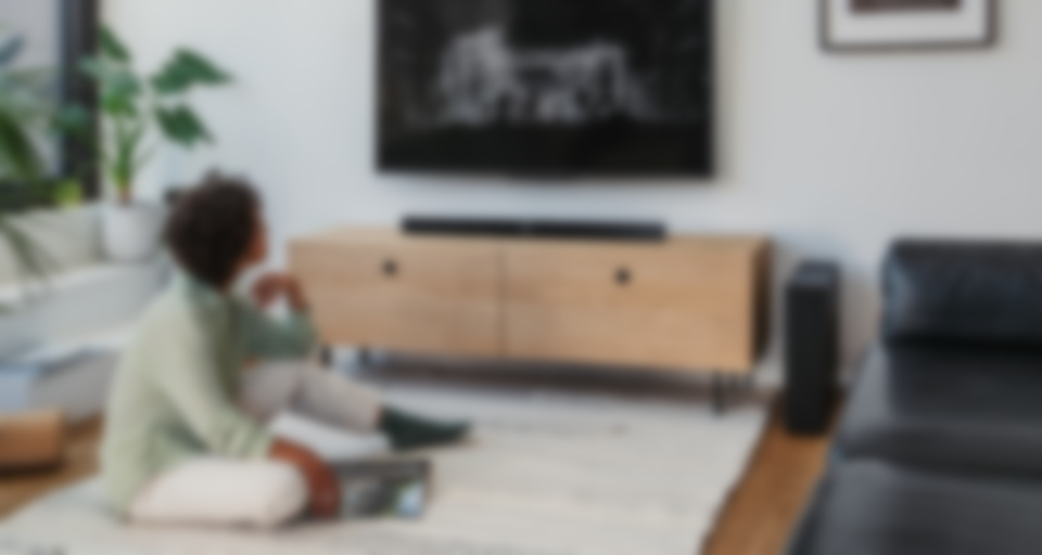 Eine Person sitzt auf einem Teppich und genießt einen Film im Fernsehen, mit einer CINEBAR 11 Soundbar in einem stilvollen Wohnzimmer.