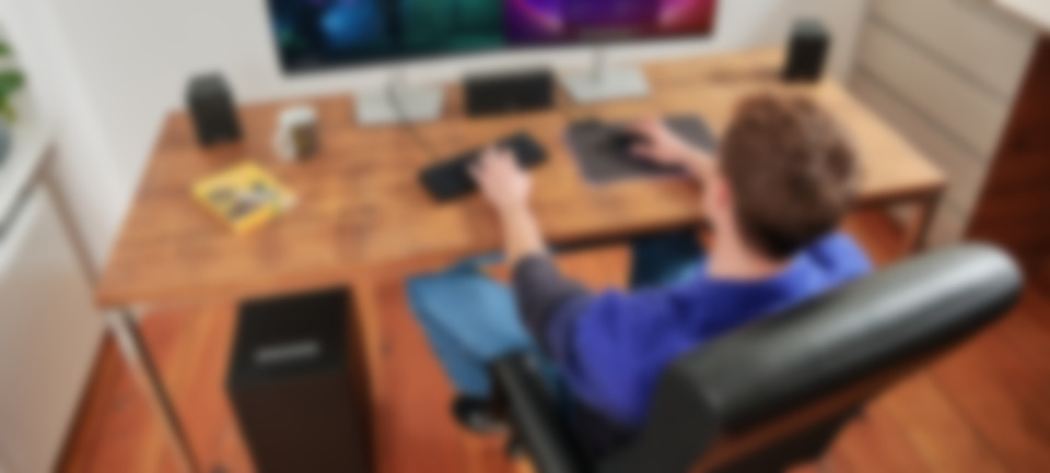 Une personne est assise à un bureau avec un ordinateur et des enceintes Surround CONSONO 25 CONCEPT dans un bureau à domicile confortable.