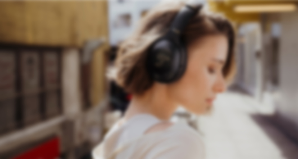 A young woman wears stylish black REAL BLUE PRO headphones outdoors.