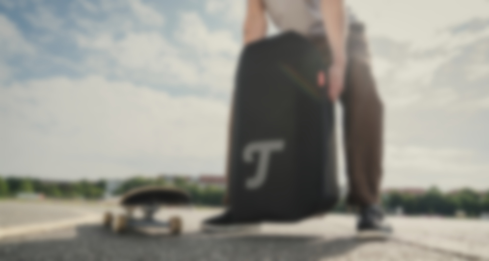 Person holding a large black bag with a logo, next to a skateboard on a sunny outdoor surface.