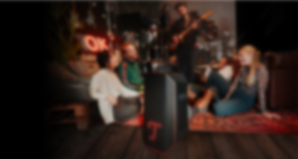 Un groupe d'amis profite de la musique en étant assis par terre, avec une enceinte portable ROCKSTER AIR 2 au premier plan.