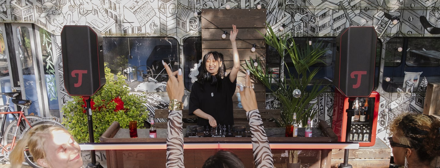 A DJ performs at an outdoor event, surrounded by two ROCKSTER AIR 2.
